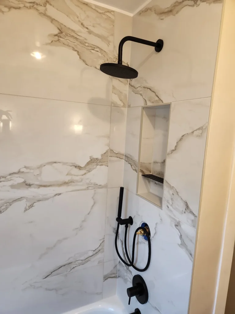 Marble-look shower wall tile with a recessed niche and black fixtures